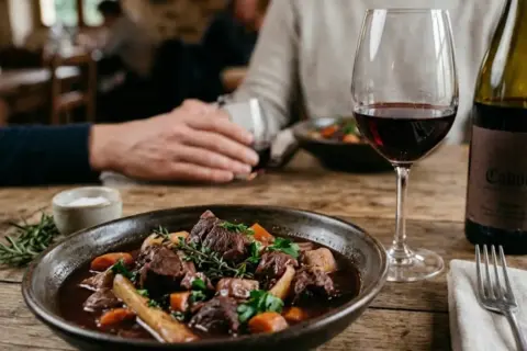 Un plat de sanglier en sauce, garni d'herbes, servi avec un verre de vin rouge et une bouteille de Cahors. Parfait pour savoir quel vin avec sanglier en sauce.