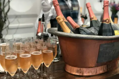 Une belle quantité de vin pour un mariage, avec des flûtes remplies de champagne et des bouteilles au frais dans un grand seau en cuivre.