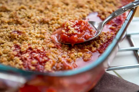Une cuillère prélève une portion généreuse de crumble rhubarbe, révélant la garniture fruitée et croustillante.