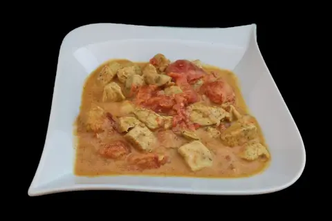 Un plat de poulet curry coco crémeux avec des morceaux de poulet tendre et des tomates, servi dans une assiette blanche.