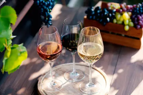 Trois verres de vin, un rosé, un rouge et un blanc pétillant, évoquent la dégustation de grands crus bordeaux, avec des grappes de raisin en arrière-plan.