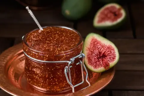 Un bocal de confiture de figues maison, avec des figues fraîches coupées en deux à côté.
