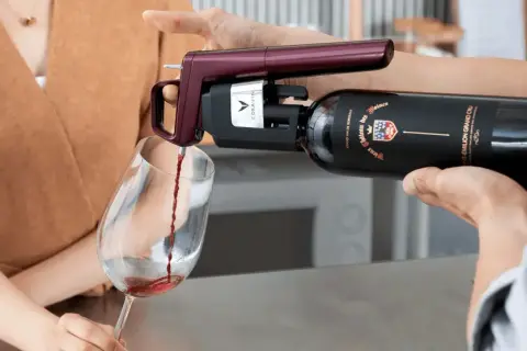 Un appareil Coravin sert un vin rouge d'une bouteille ouverte dans un verre, assurant sa conservation.