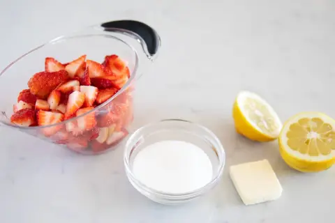 Ingrédients pour un coulis de fraise : fraises coupées, sucre, beurre et citrons.