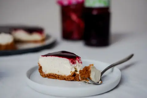 Une part de cheesecake sans cuisson crémeux, nappé de coulis de fruits rouges, sur une assiette blanche. Une bouchée est prélevée à la fourchette.