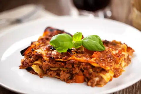 Une part de lasagnes à la bolognaise, garnie de basilic frais. Idéal pour savoir quel vin avec des lasagnes.