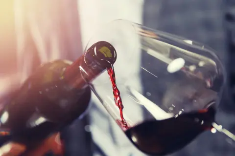 Un vin rouge acide est versé d'une bouteille dans un verre. La lumière dorée illumine la scène.