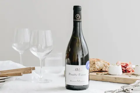 Bouteille de vin blanc Pouilly-Fuissé, prête pour un mariage. Deux verres à vin vides, du fromage de chèvre et du pain sur une planche.