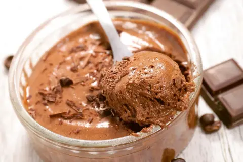 Une cuillère prélève une portion aérienne de mousse au chocolat, garnie de copeaux de chocolat. Un délice gourmand.