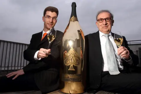 Deux hommes en costume célèbrent avec une gigantesque bouteille de champagne dorée, une véritable bouteille Midas.
