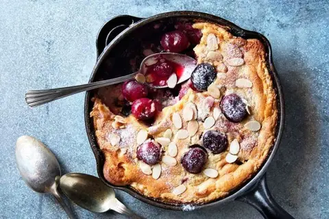 Clafoutis aux cerises dans une poêle, saupoudré de sucre glace et d'amandes effilées. Une recette clafoutis facile et gourmande.