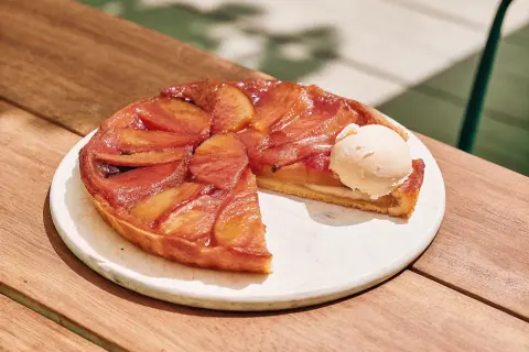 Tarte Tatin aux pommes caramélisées avec une boule de glace à la vanille sur une assiette blanche.