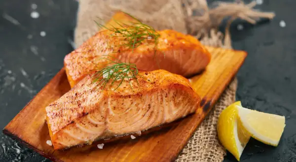 Deux pavés de saumon grillé, ornés d'aneth et de gros sel, servis sur une planche en bois avec des quartiers de citron. Un délice pour accompagner un bon vin.