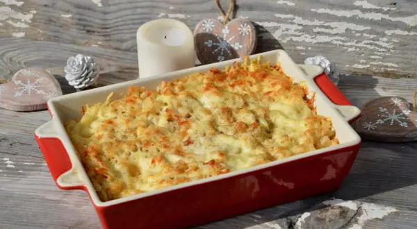 Un plat de gratin de crozet doré et gratiné, prêt à être dégusté. Une bougie et des décorations en bois en forme de cœur complètent la scène hivernale.