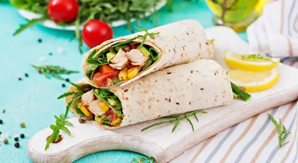 Deux wraps au poulet garnis de légumes frais, servis sur une planche en bois avec des quartiers de citron.