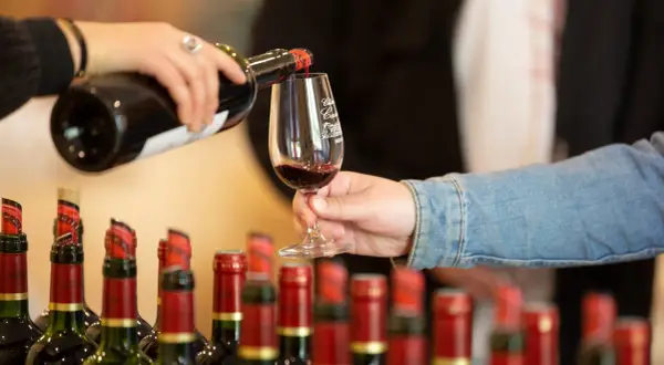 Service d'un vin rouge pour l'apéro, avec des bouteilles alignées en arrière-plan.
