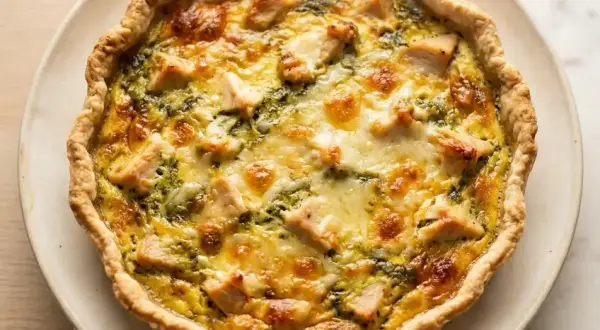 Une délicieuse quiche au poulet, dorée et garnie de morceaux de poulet et de fromage fondant, prête à être dégustée.