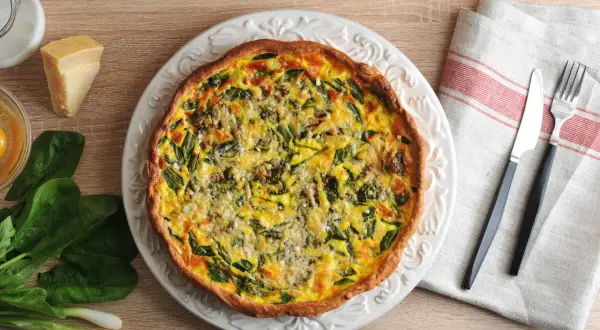 Une appétissante quiche aux légumes, garnie d'épinards et de fromage, prête à être dégustée.