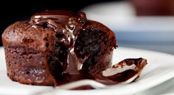 Un fondant au chocolat dégoulinant de sauce, une cuillère prête à savourer ce délice.