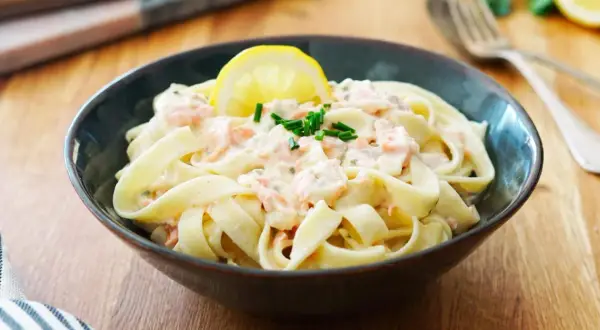 Un plat de tagliatelles au saumon crémeuses, garni d'une tranche de citron et de ciboulette fraîche. Un délice pour les papilles.