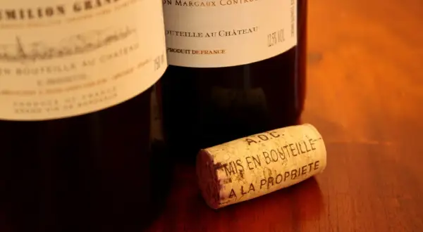 Bouchon de liège marqué "A.O.C. Mis en bouteille à la propriété", près de bouteilles de vin français, dont une de Margaux.