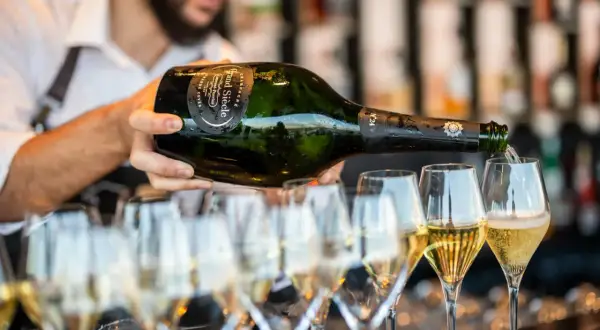 Un serveur verse du champagne d'une bouteille magnum dans plusieurs flûtes. La quantité de champagne est généreuse.