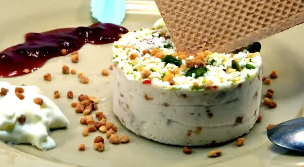 Un délicieux nougat glacé, parsemé de fruits secs et de pistaches, servi avec une touche de coulis de fruits rouges et une gaufrette croustillante.
