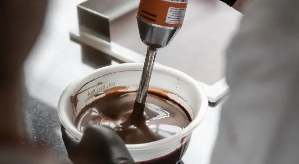 Un mixeur plongeant prépare une onctueuse ganache chocolat dans un bol.