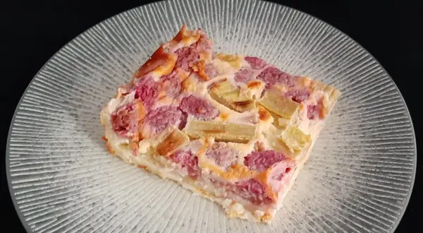 Tranche de clafoutis rhubarbe aux fruits rouges, sur une assiette transparente aux motifs rayonnants.
