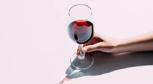 Une main tient délicatement un verre de vin rouge, le pouce et l'index sur le pied. Apprenez comment tenir un verre de vin pour en apprécier toutes les saveurs.