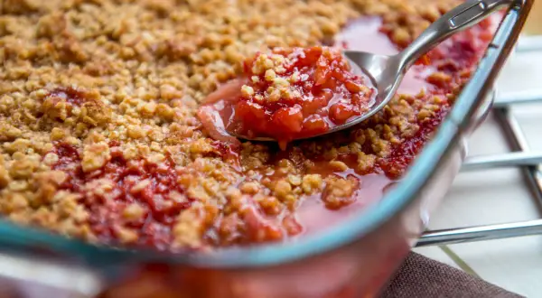 Une cuillère prélève une portion généreuse de crumble rhubarbe, révélant la garniture fruitée et croustillante.