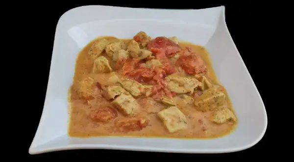 Un plat de poulet curry coco crémeux avec des morceaux de poulet tendre et des tomates, servi dans une assiette blanche.