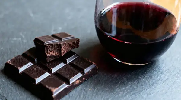 Un verre de vin rouge et des carrés de chocolat noir sur une surface sombre. Un délice pour les sens, le vin et chocolat.