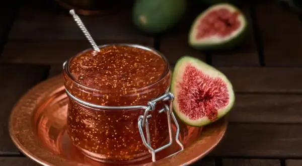 Un bocal de confiture de figues maison, avec des figues fraîches coupées en deux à côté.