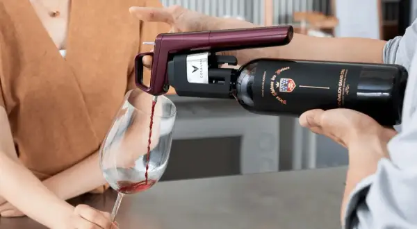 Un appareil Coravin sert un vin rouge d'une bouteille ouverte dans un verre, assurant sa conservation.