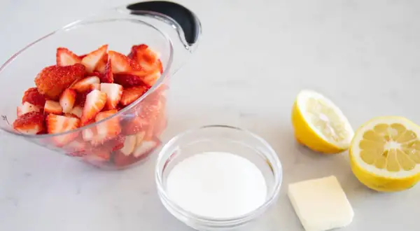 Ingrédients pour un coulis de fraise : fraises coupées, sucre, beurre et citrons.