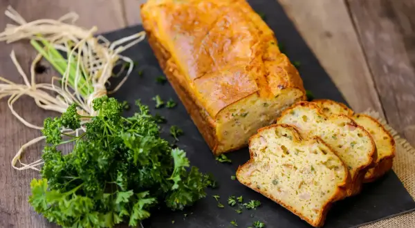 Un délicieux cake au thon, doré et moelleux, tranché et présenté avec du persil frais sur une planche d'ardoise.