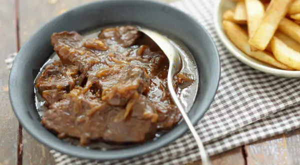 Un plat de carbonade flamande mijotée, servie dans un bol avec une cuillère, à côté d'une coupelle de frites dorées.