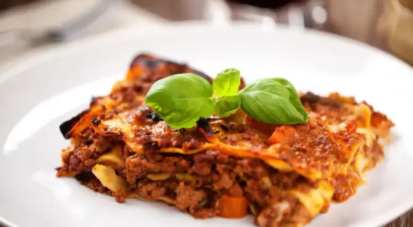 Une part de lasagnes à la bolognaise, garnie de basilic frais. Idéal pour savoir quel vin avec des lasagnes.
