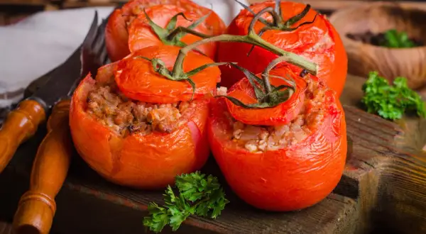 Quatre tomates farcies appétissantes, garnies d'une farce savoureuse, reposent sur une planche en bois rustique.