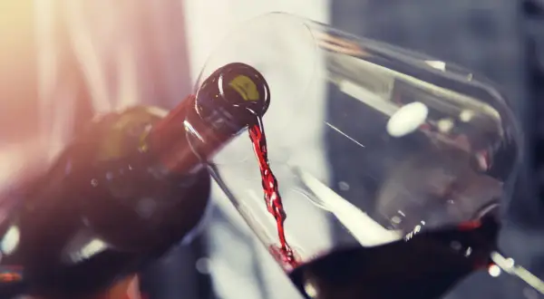Un vin rouge acide est versé d'une bouteille dans un verre. La lumière dorée illumine la scène.