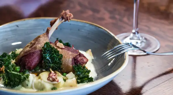 Un plat de cuisse de canard confite, servi avec des légumes verts croquants et une purée onctueuse. Un verre de vin rouge à proximité suggère un accord parfait.