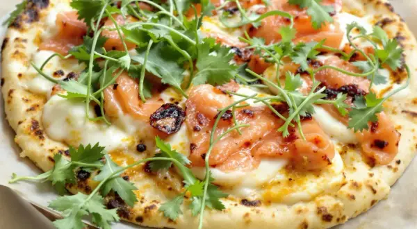 Une délicieuse pizza saumon, garnie de fromage fondant et de coriandre fraîche. Un vrai régal pour les yeux et les papilles !