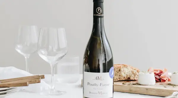 Bouteille de vin blanc Pouilly-Fuissé, prête pour un mariage. Deux verres à vin vides, du fromage de chèvre et du pain sur une planche.