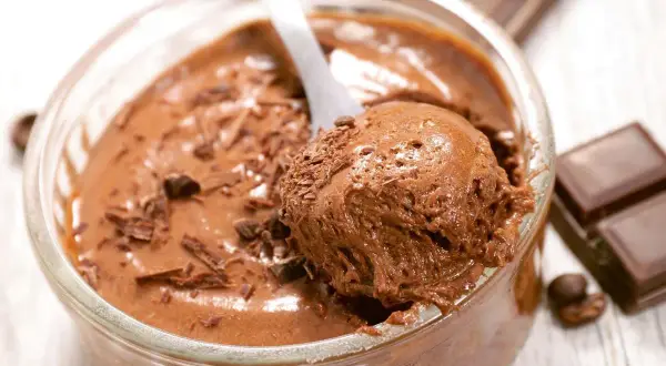 Une cuillère prélève une portion aérienne de mousse au chocolat, garnie de copeaux de chocolat. Un délice gourmand.