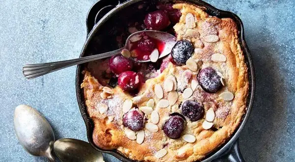 Clafoutis aux cerises dans une poêle, saupoudré de sucre glace et d'amandes effilées. Une recette clafoutis facile et gourmande.