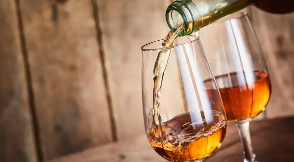 Un verre se remplit d'un vin paillé ambré, un autre verre est déjà servi. Ambiance chaleureuse sur fond de bois.