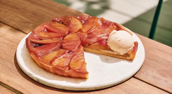 Tarte Tatin aux pommes caramélisées avec une boule de glace à la vanille sur une assiette blanche.