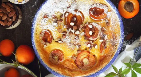 Un délicieux flan aux abricots, saupoudré de sucre glace et parsemé d'amandes concassées, prêt à être dégusté.
