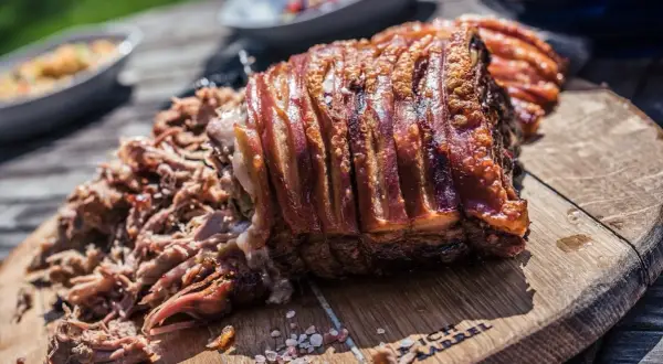 Un morceau de porc rôti avec une couenne croustillante et un effiloché de porc savoureux sur une planche en bois.